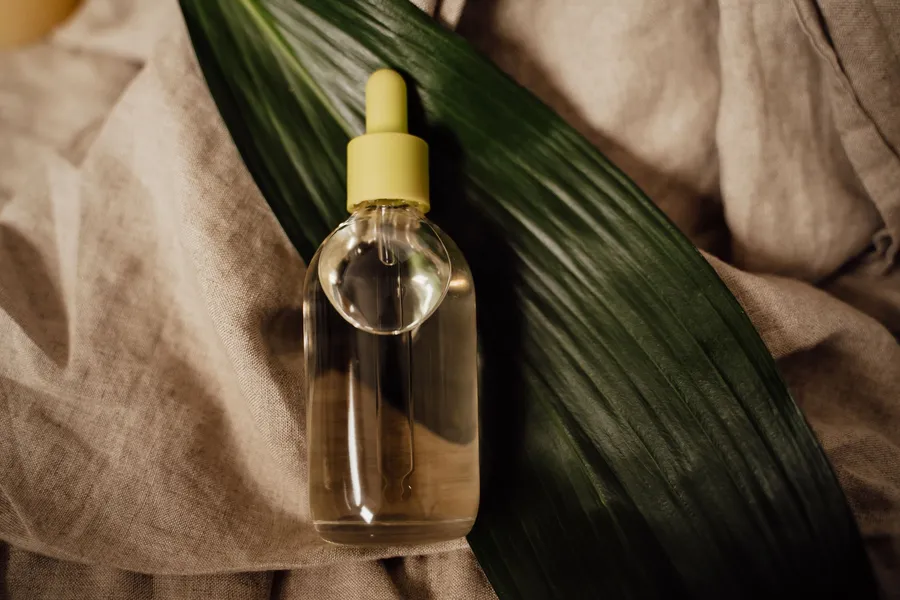 Glass dropper bottle on a green leaf and soft linen